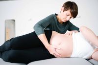 Eine Osteopathin behandelt den Bauch einer schwangeren Frau.