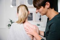 Eine Osteopathin behandelt die Schulter einer jungen Frau.